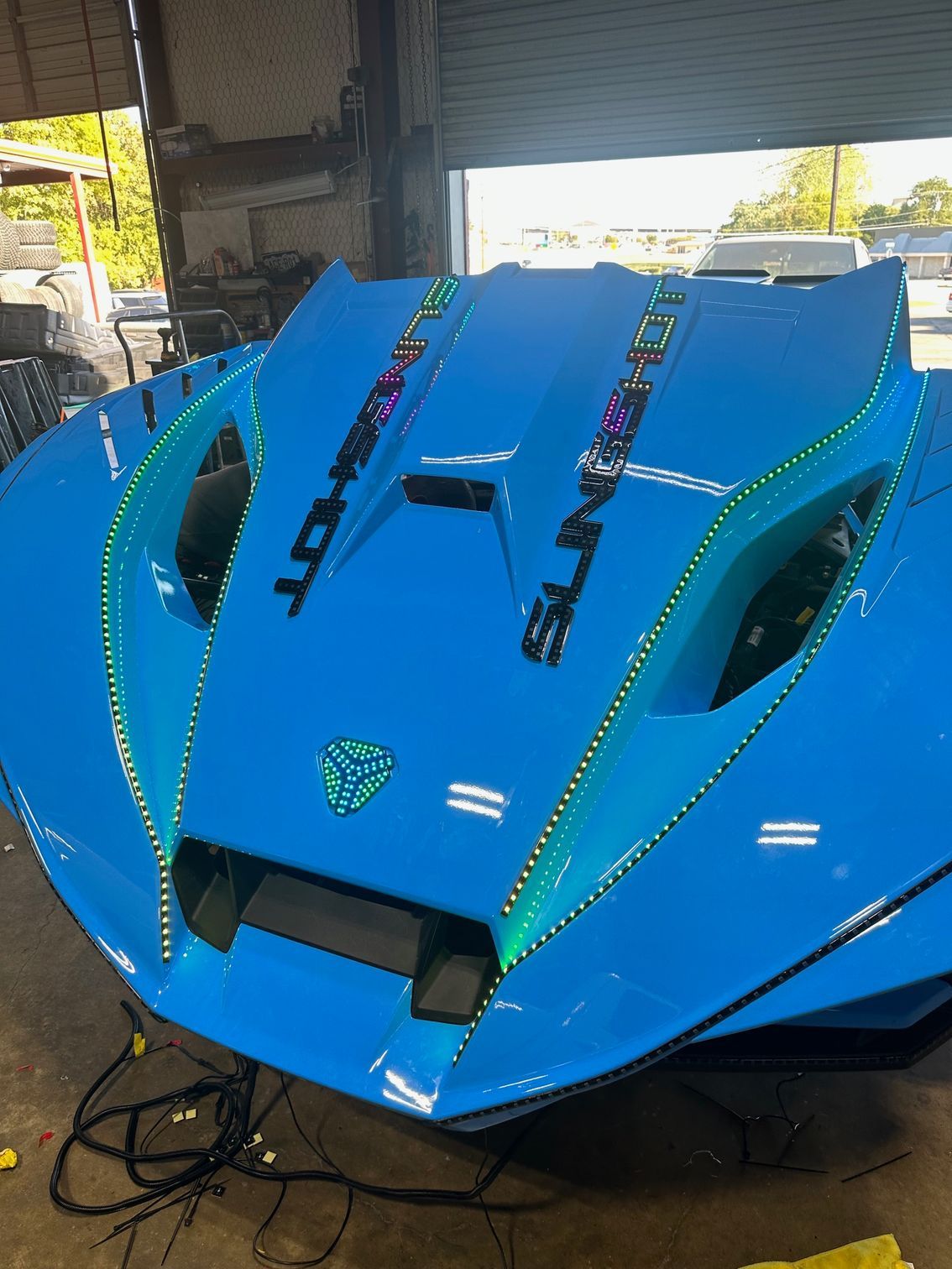 Bright blue Polaris Slingshot with LED lights, parked indoors.