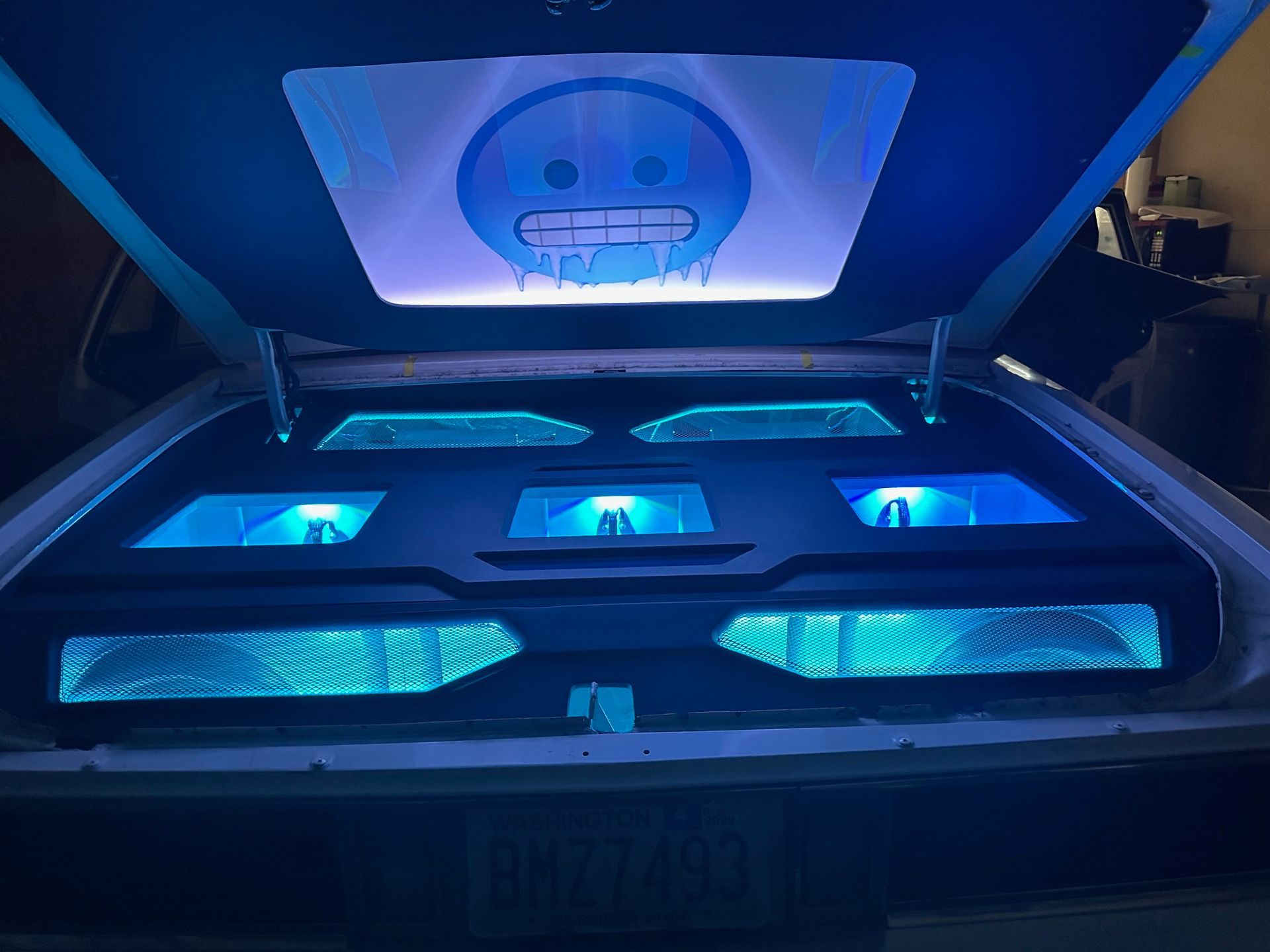 Car trunk with blue LED lights illuminating a speaker system, including an emoji.