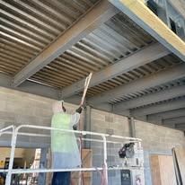Person in safety vest painting metal ceiling with a long handled tool, construction site.