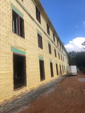 Building exterior under construction with exposed yellow insulation, windows, and a gravel path.