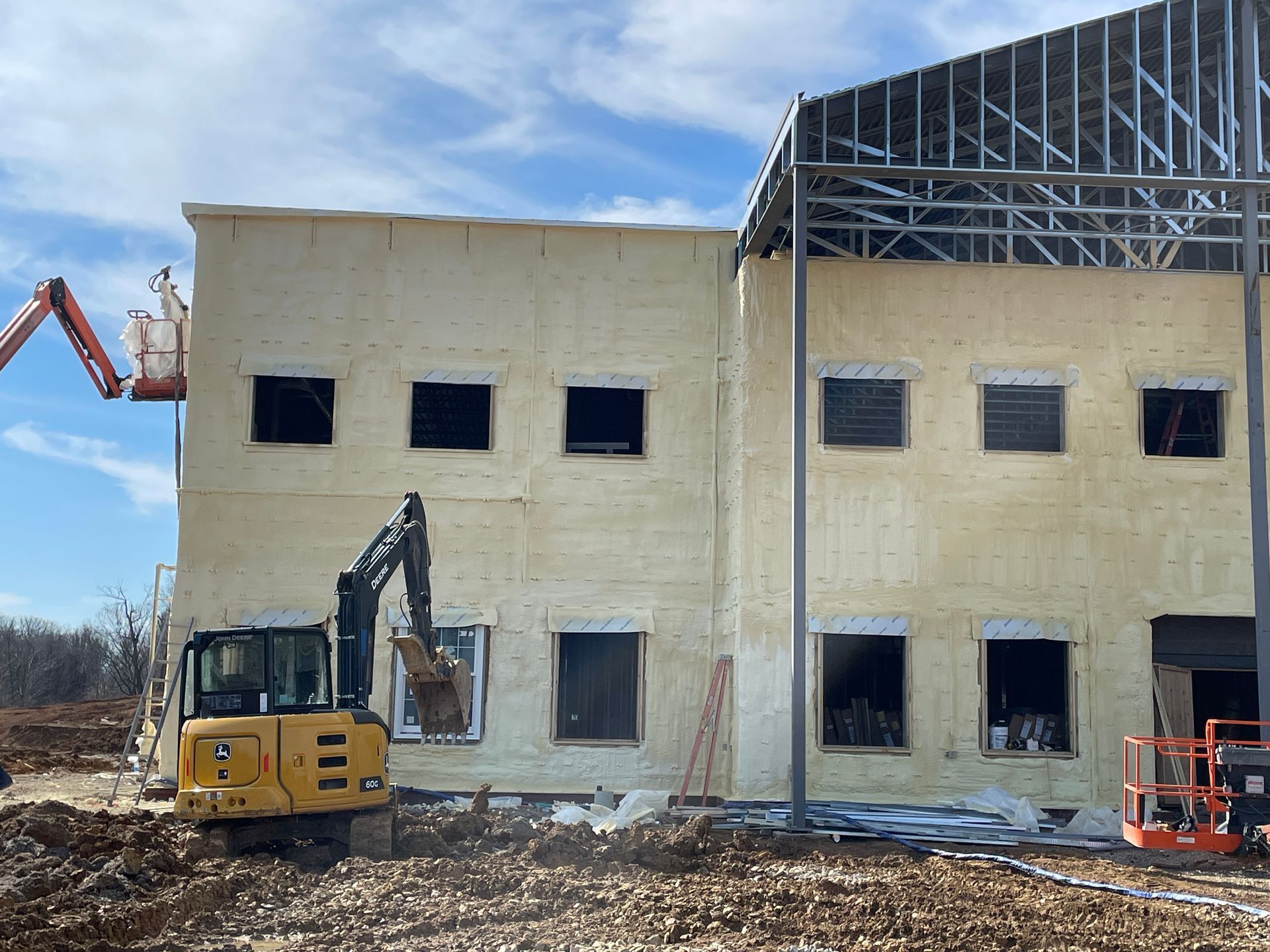 Construction site: yellow excavator, partially built building with window openings, sky.