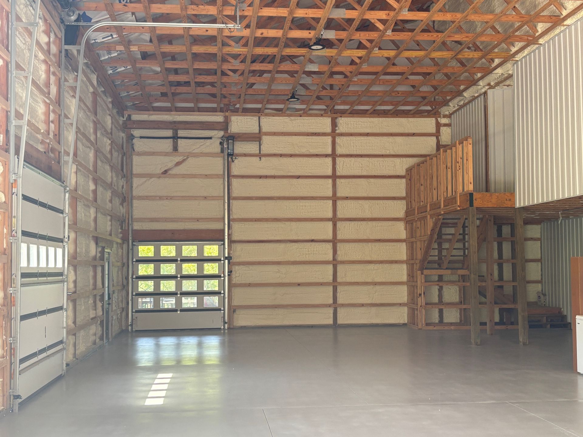 Empty warehouse interior with exposed wooden beams, open garage door, and a mezzanine.