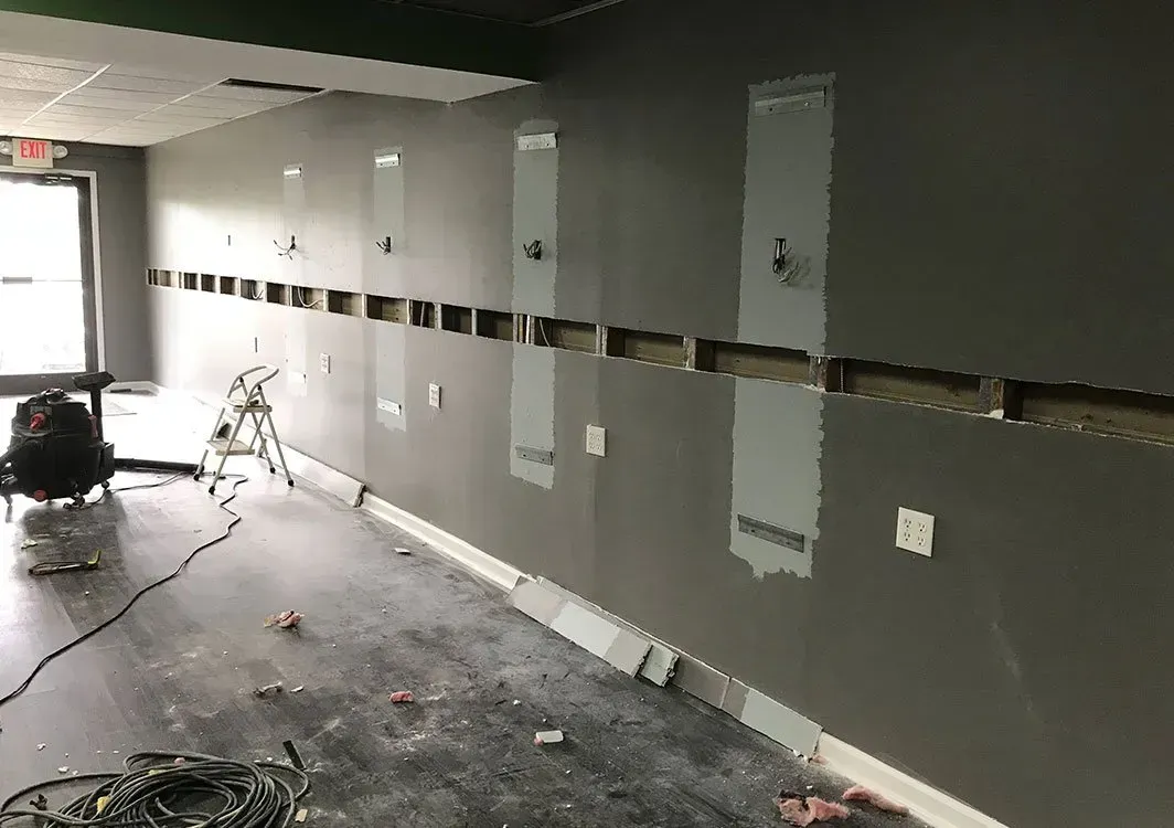 Interior wall under construction with rectangular cutouts for electrical. Gray paint, unfinished floor.