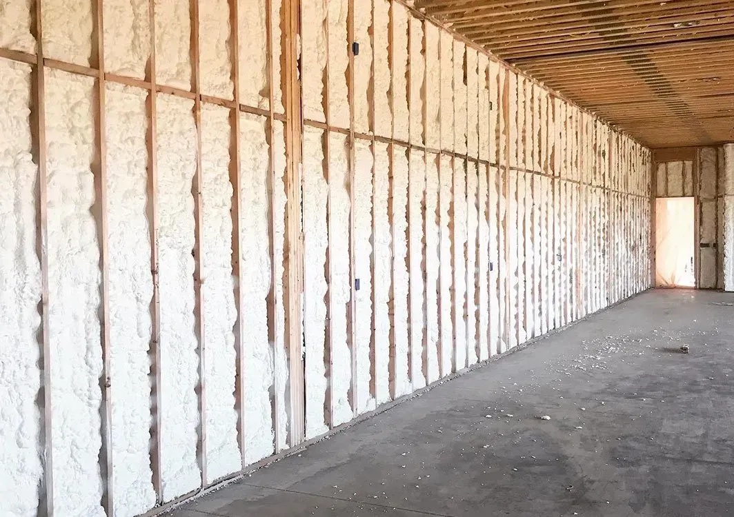Interior view of a building's unfinished walls, insulated with white foam between wooden studs; a concrete floor.