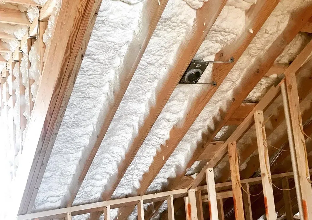 Ceiling with insulation between wooden beams, near unfinished wall.