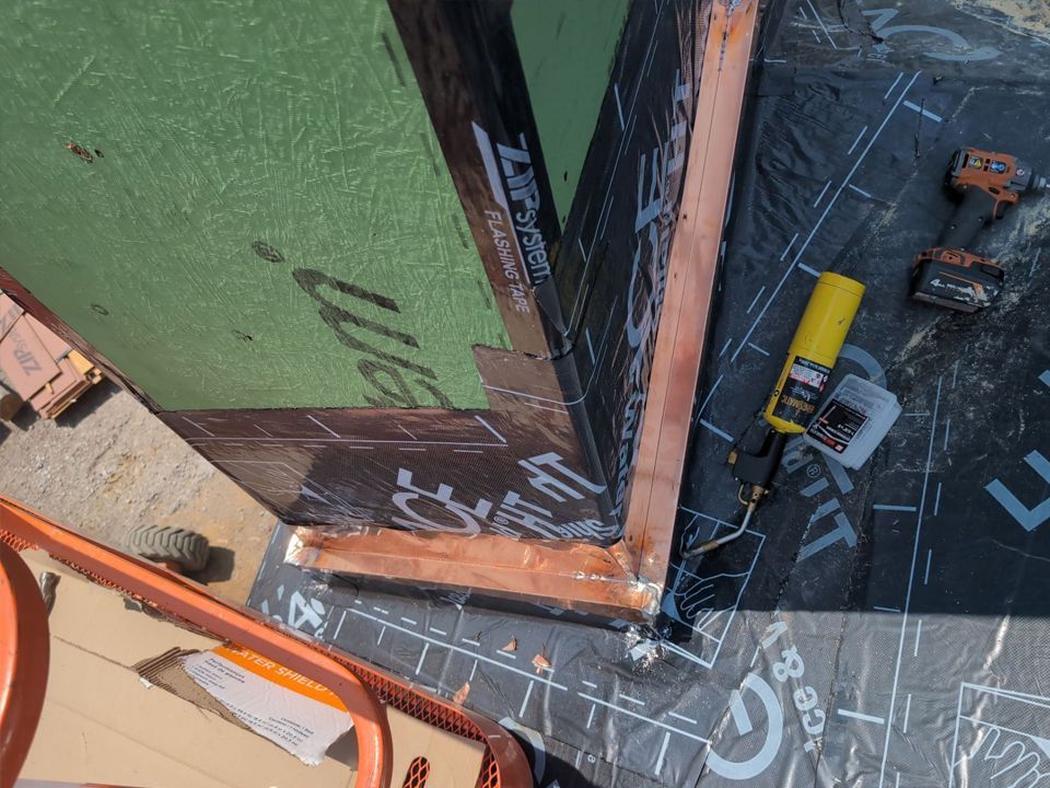 Construction of a corner roof detail with copper flashing, black underlayment, and green sheathing.