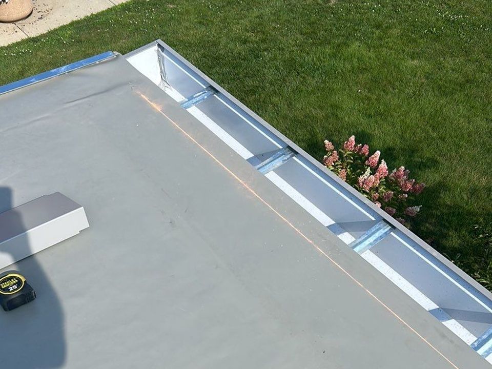 Gray flat roof with metal edging, tape measure, and green grass in the background.