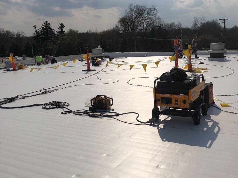 Roofing crew working on a white flat roof, with equipment and safety cones.