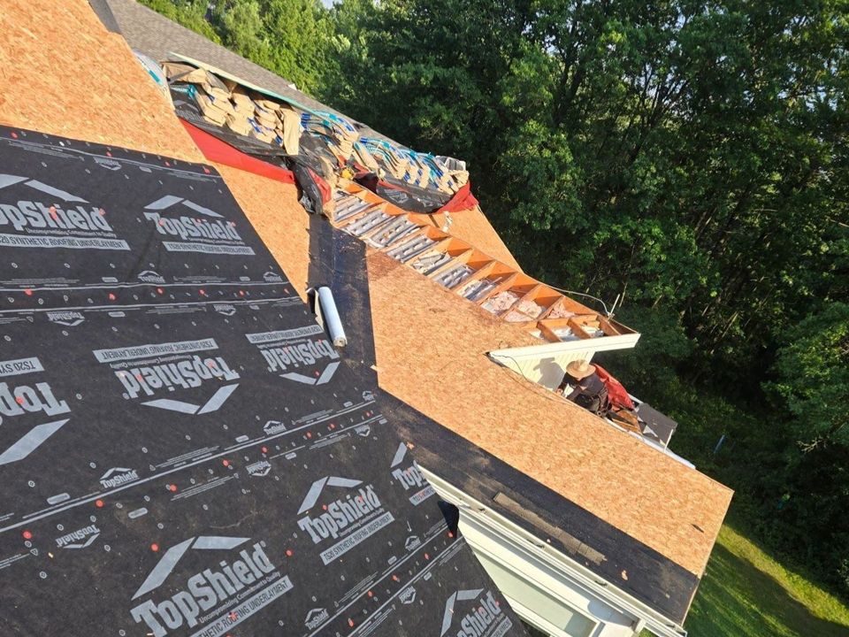Workers install black underlayment on a wooden roof structure, with some sections exposed and others partially covered.