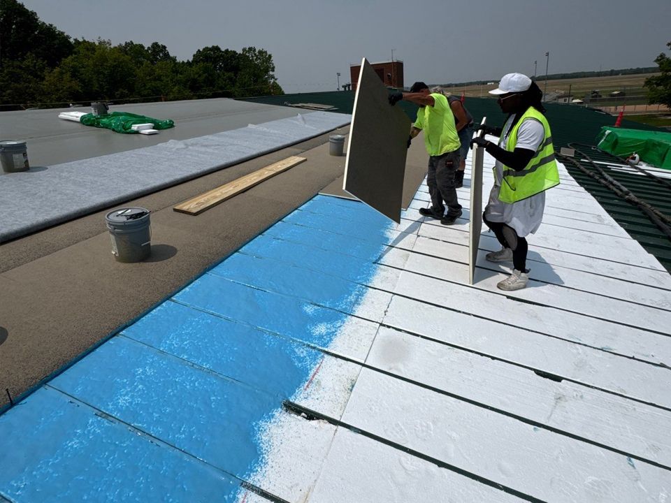 Two workers installing a section of roof insulation. Blue coating, light-colored insulation, and a flat roof are visible.