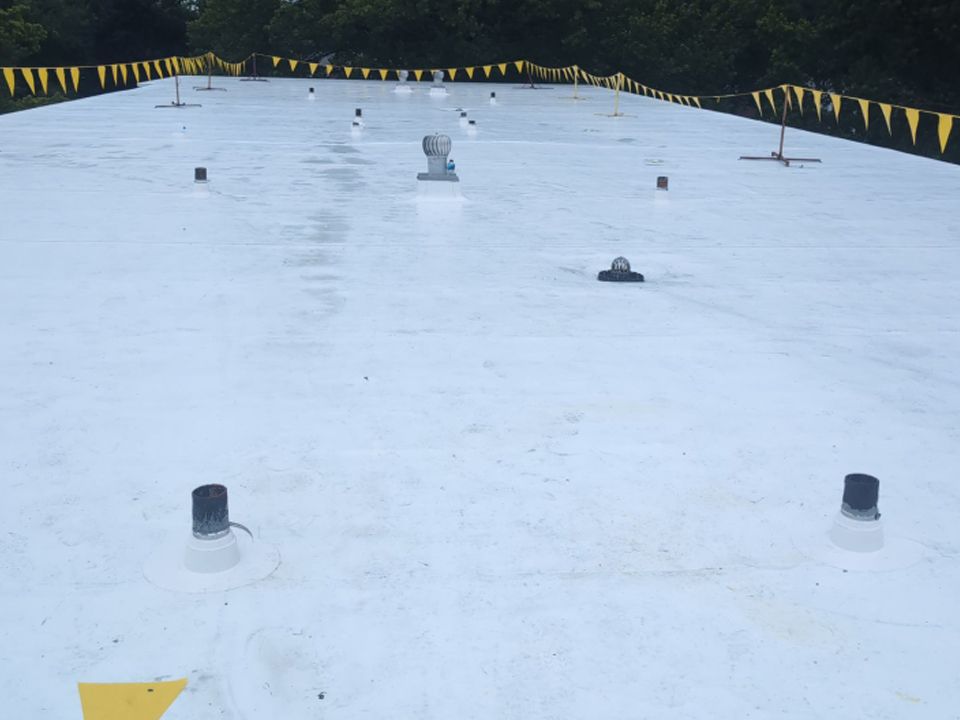 White flat roof with black vents and yellow safety flags in a forest setting.