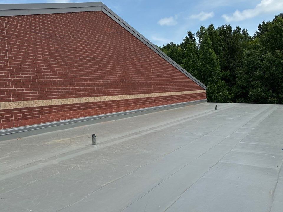 Red brick building with flat, gray roof. Trees in background, blue sky.
