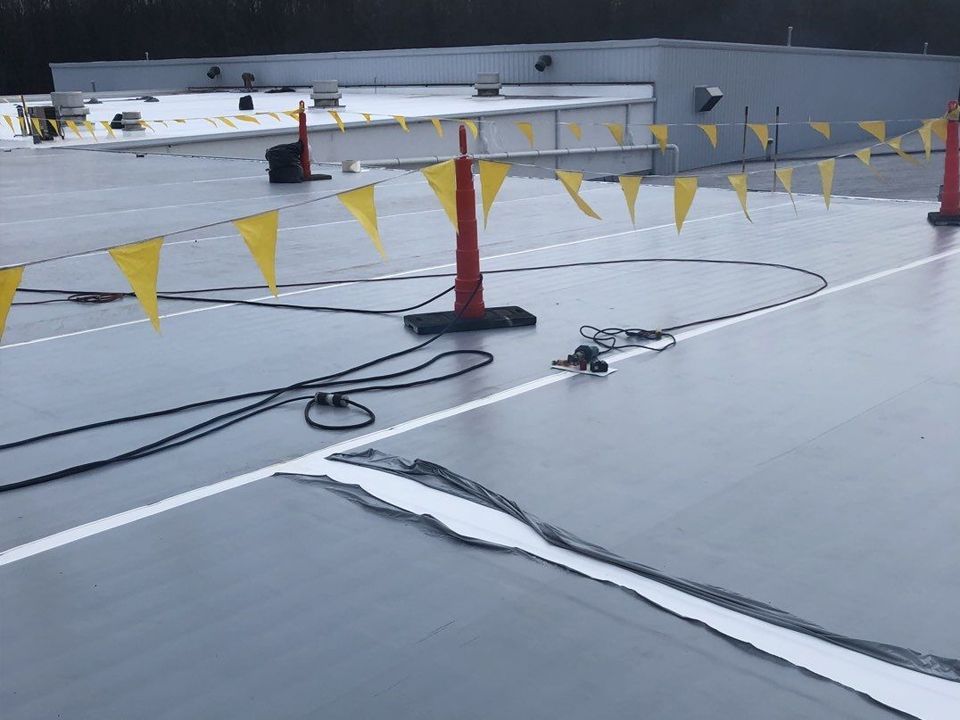 Rooftop with black and white surface, orange cones with yellow flags, and black cables.