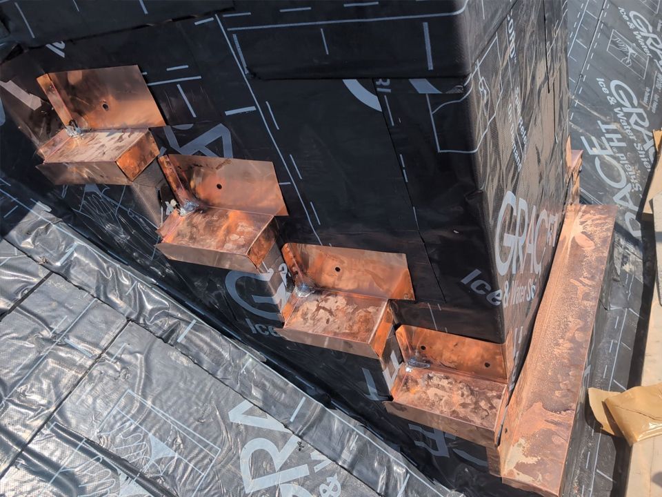 Copper step flashing installed on a roof, ready for shingles, over black waterproof membrane.