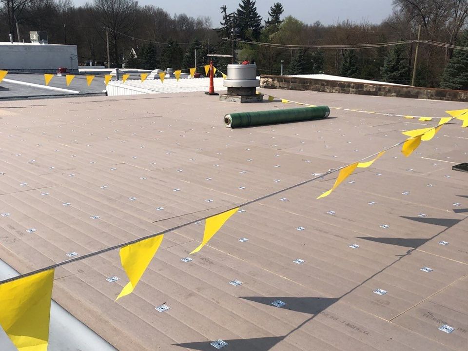 Rooftop with installed tan decking, safety flags, a roll of material, and vents.