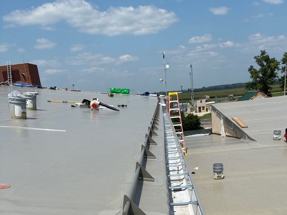 Gray roof with ladder, tools, and a metal gutter along the edge, outdoors on a sunny day.