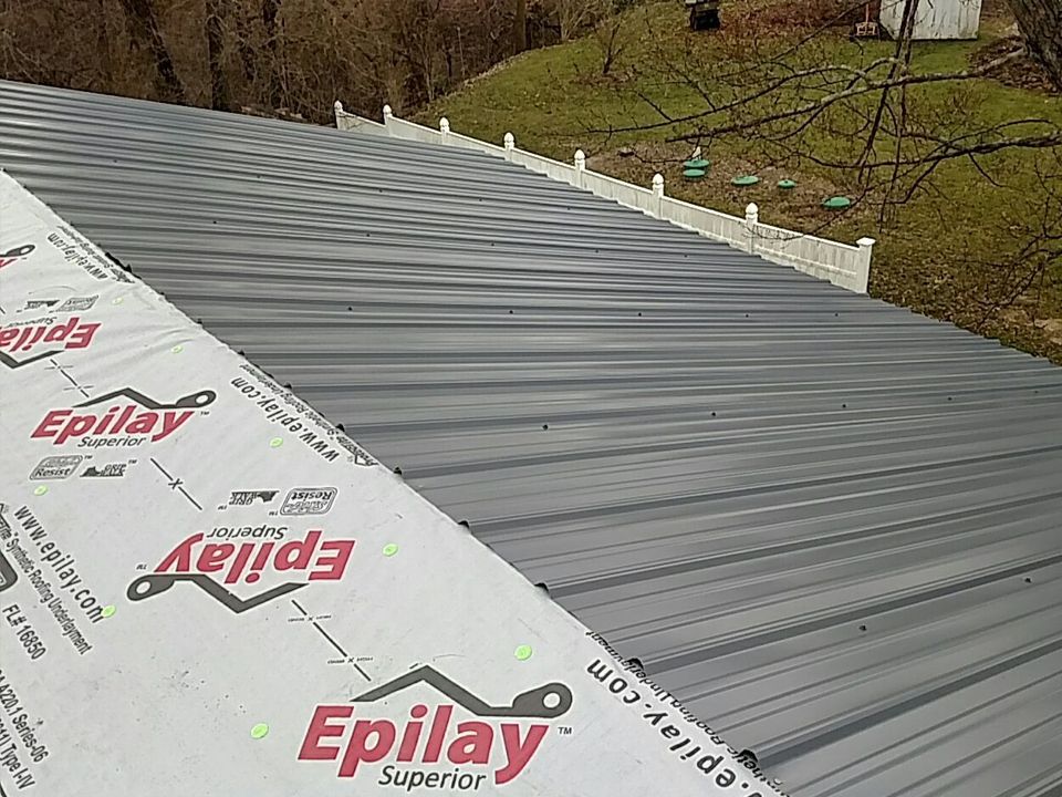 Metal roof with Epilay underlayment, viewed from above, with a white fence and green trees in the background.