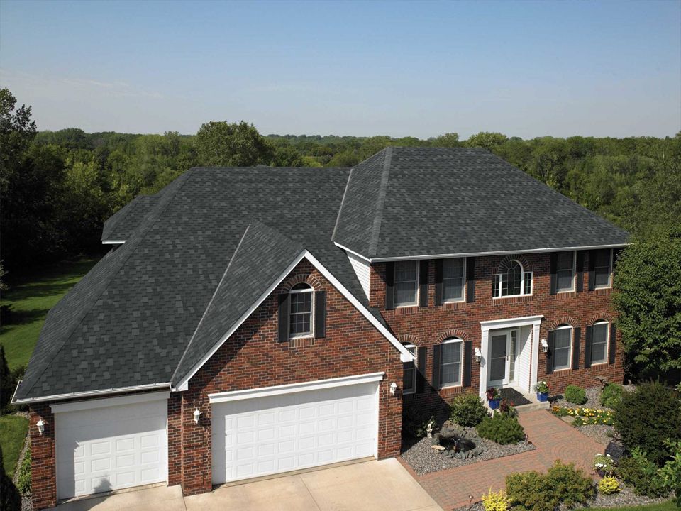 Two-story brick house with a dark gray shingle roof, white trim, and a three-car garage.