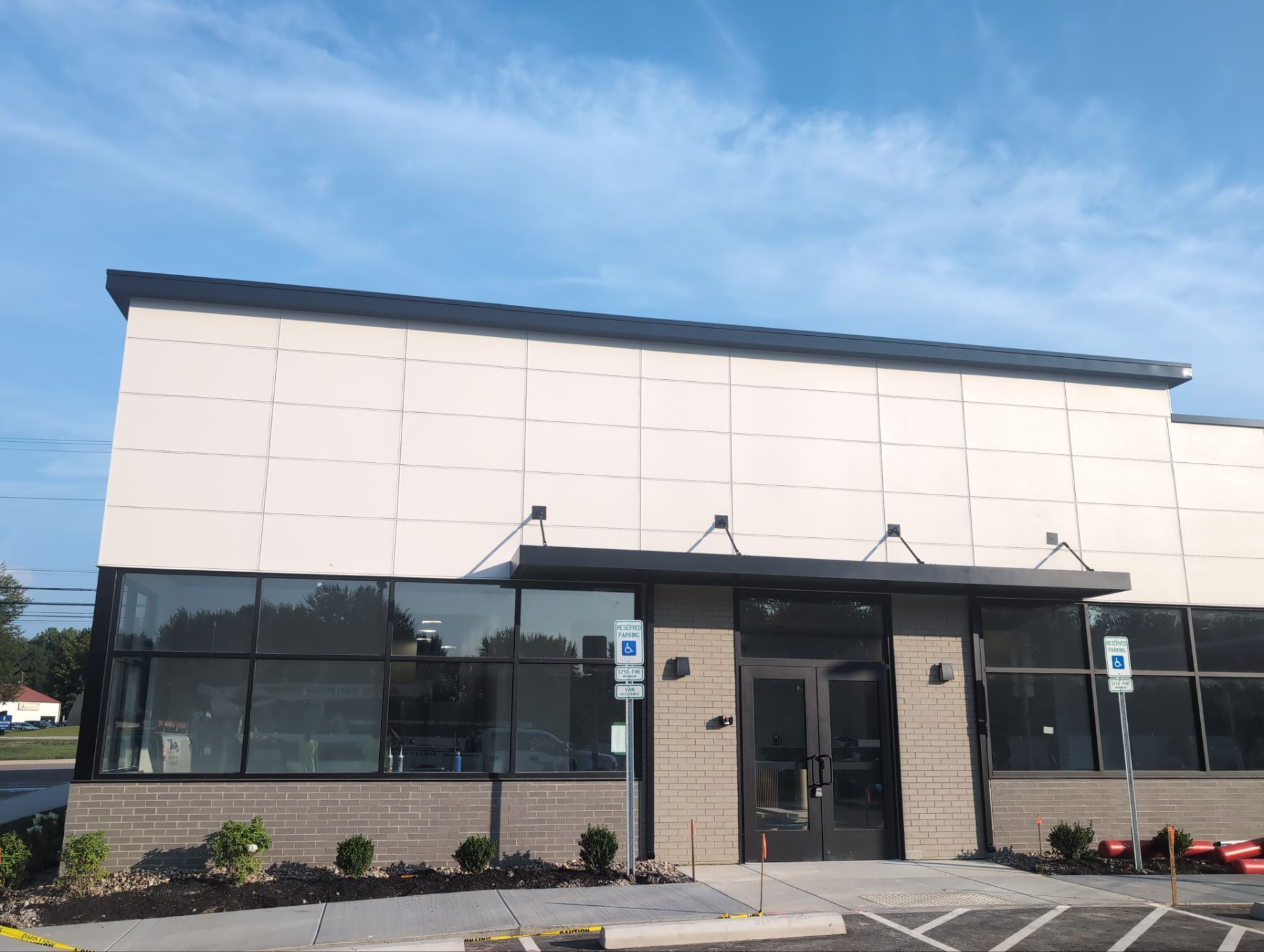 Exterior of a modern building with large windows and a dark canopy over the entrance. A handicap sign is visible.