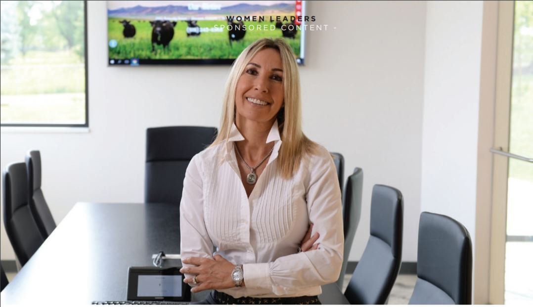 Woman in a white shirt smiles, arms crossed, in a modern conference room.