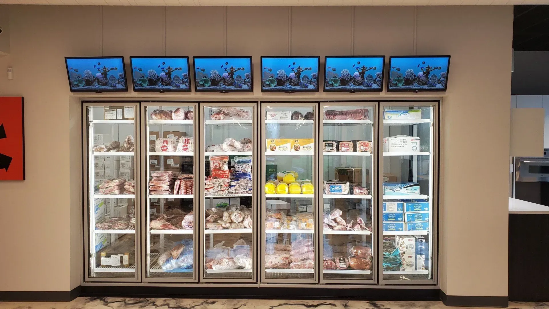 Freezer display with glass doors, stocked with frozen food, with screens above.