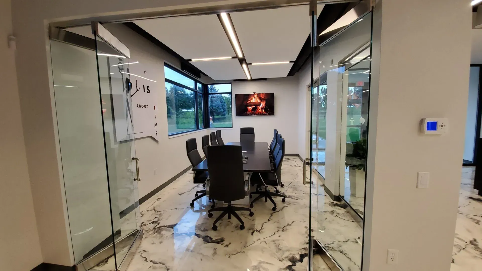 Conference room with glass walls, long table, chairs, and a TV; modern design.