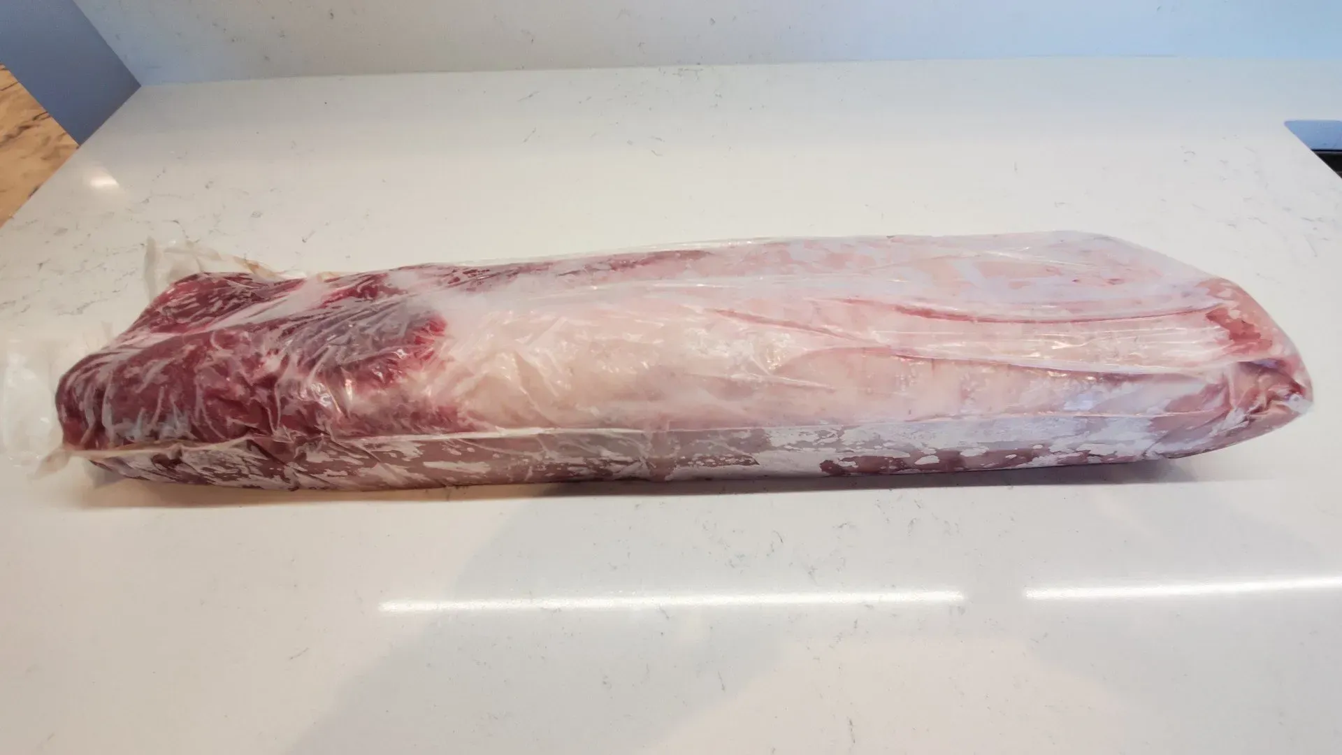 Beef roast, wrapped in clear plastic, resting on a white countertop.