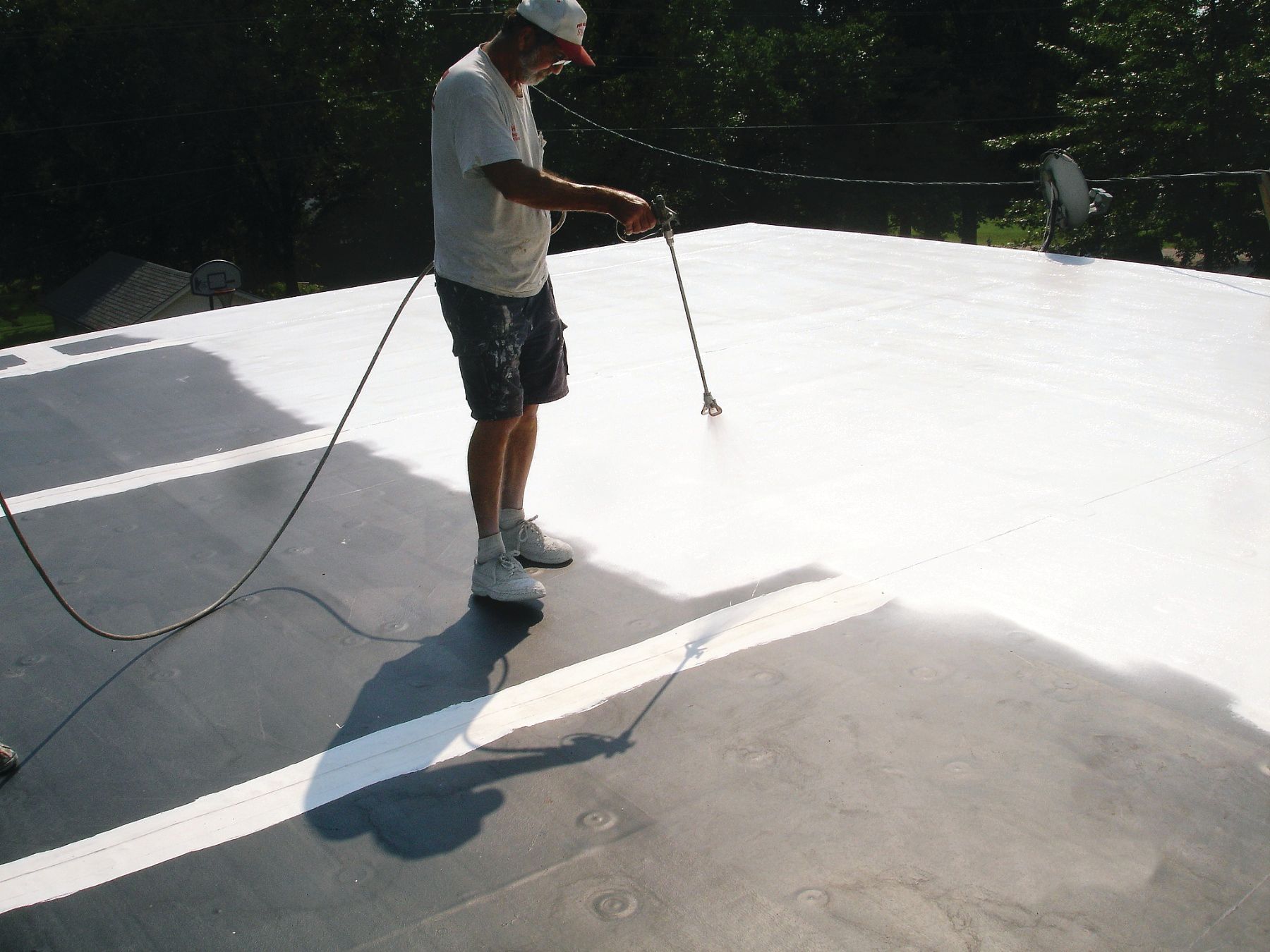A man is spraying white paint on a roof