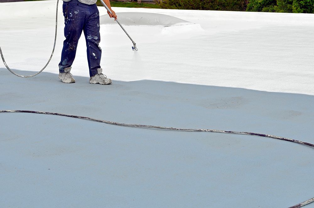 A man is painting a roof with a sprayer.
