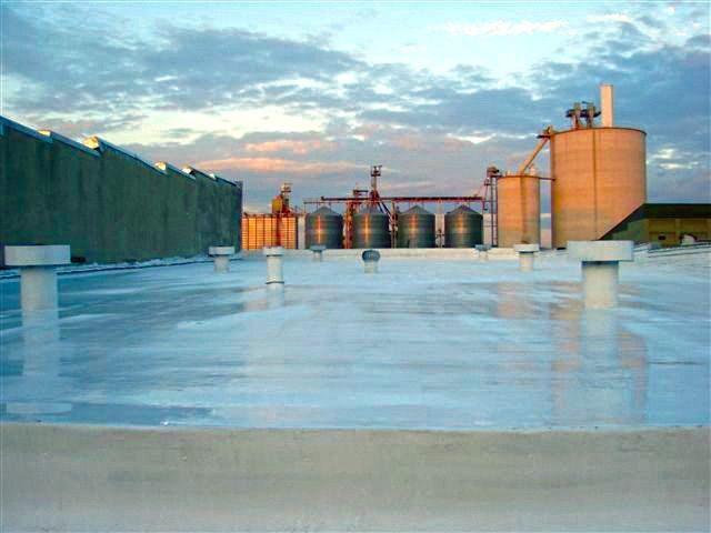 A rooftop view of a factory with silos and a sunset in the background.