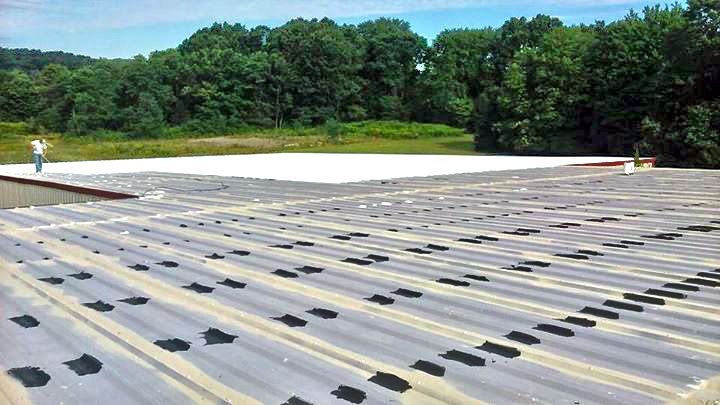 A man is standing on top of a roof with trees in the background.