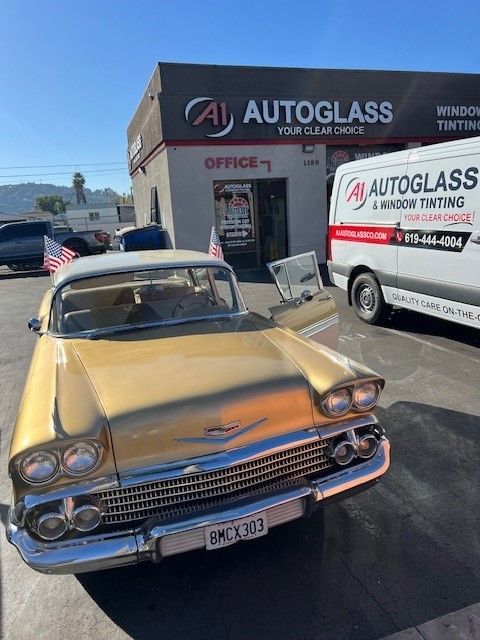 A yellow car is parked in front of an autoglass store.