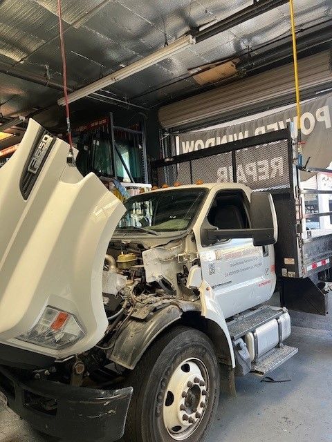 A white truck with its hood up in a garage.