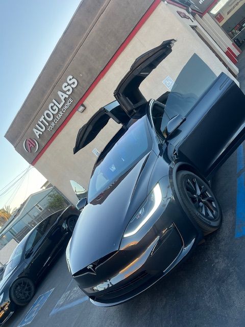 A tesla model s with its doors open is parked in front of a building that says autoglass
