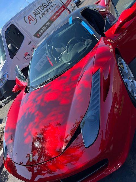 A red sports car is parked next to a white van that says aj autoglas