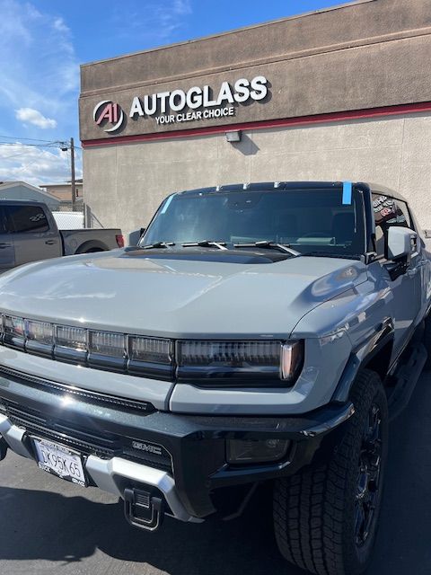 A hummer is parked in front of a building that says autoglass.