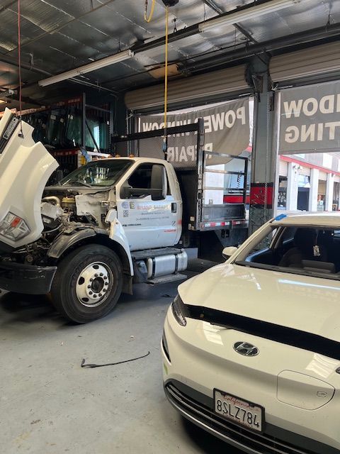 A white car is parked next to a white truck with the hood up