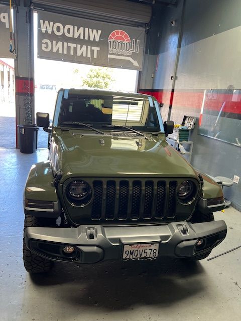 A green jeep is parked in front of a garage door.