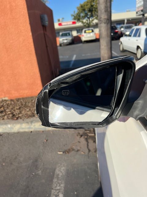 A car with a broken side mirror is parked in a parking lot