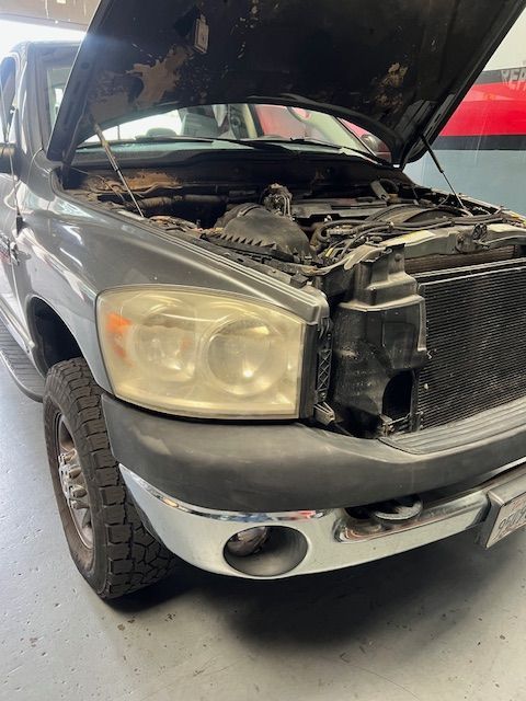 A dirty truck with the hood up is parked in a garage.