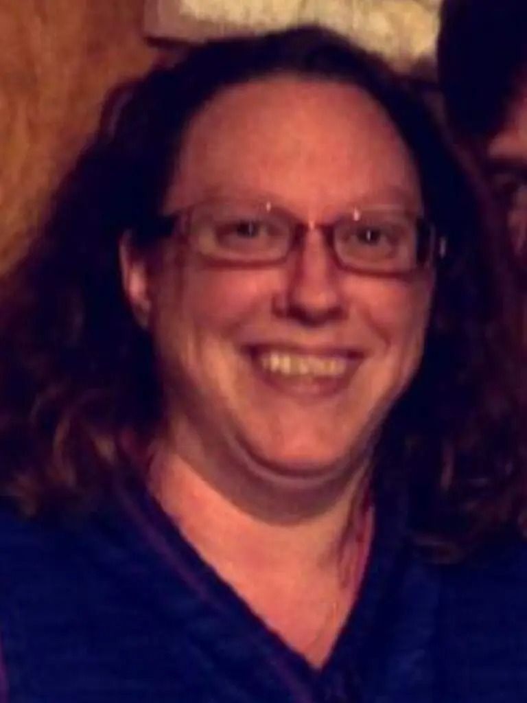 A woman wearing glasses and a blue shirt smiles for the camera