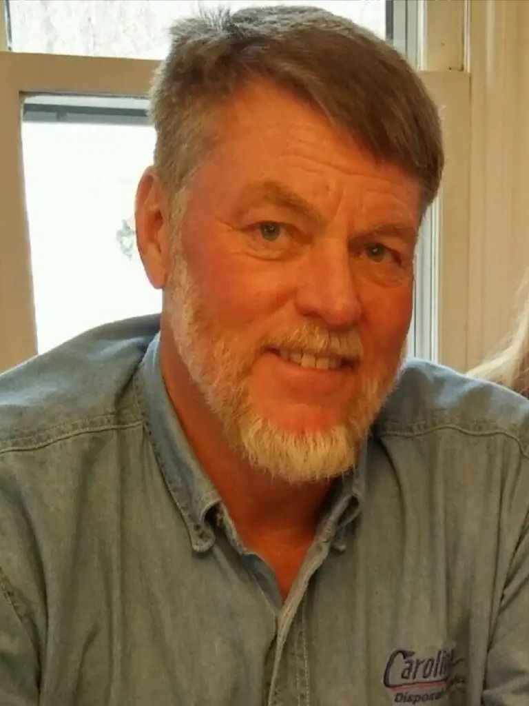 A man with a beard is wearing a blue shirt and smiling.