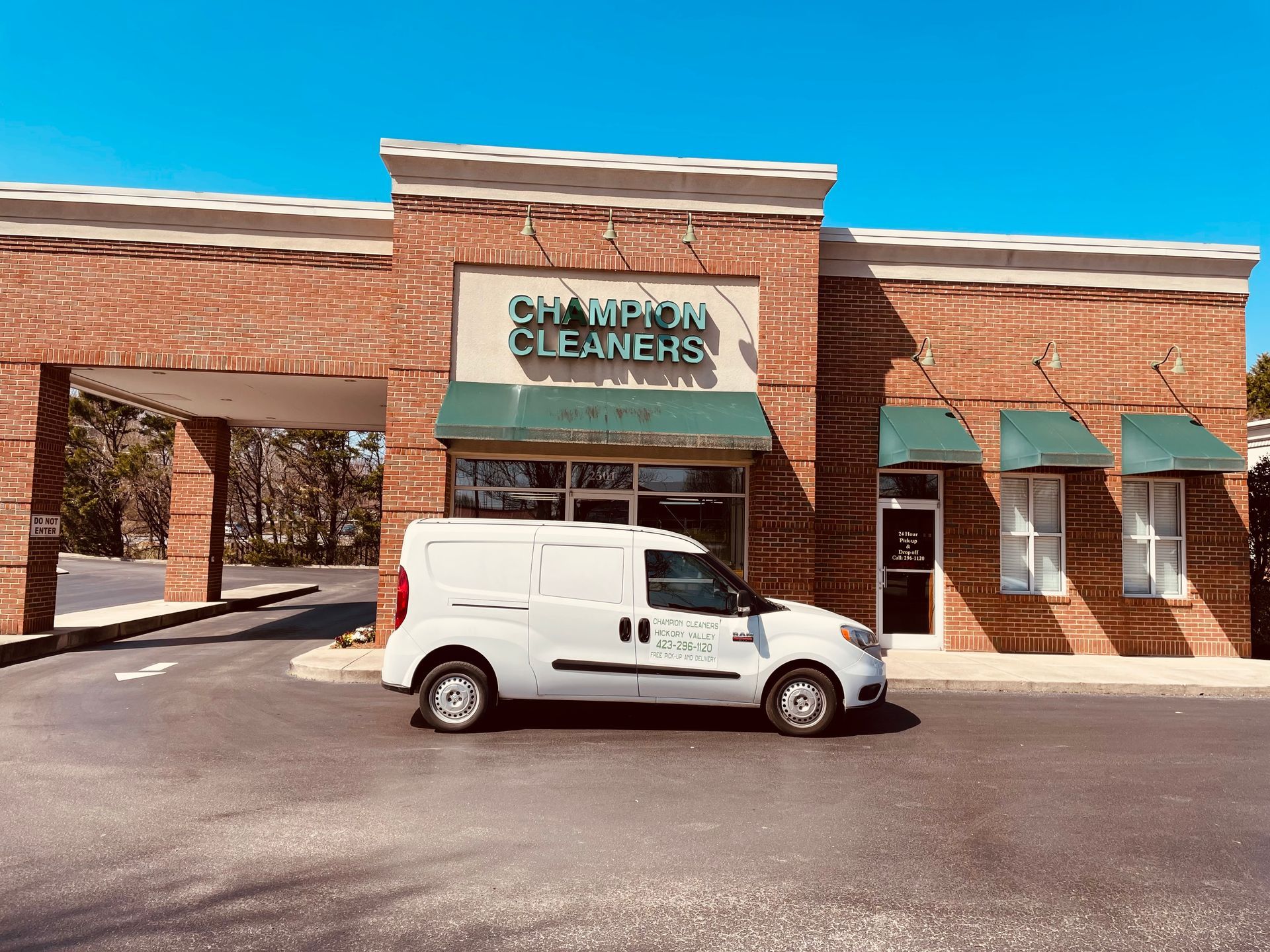 White Champion Cleaners van parked in front of a brick building under a clear blue sky.