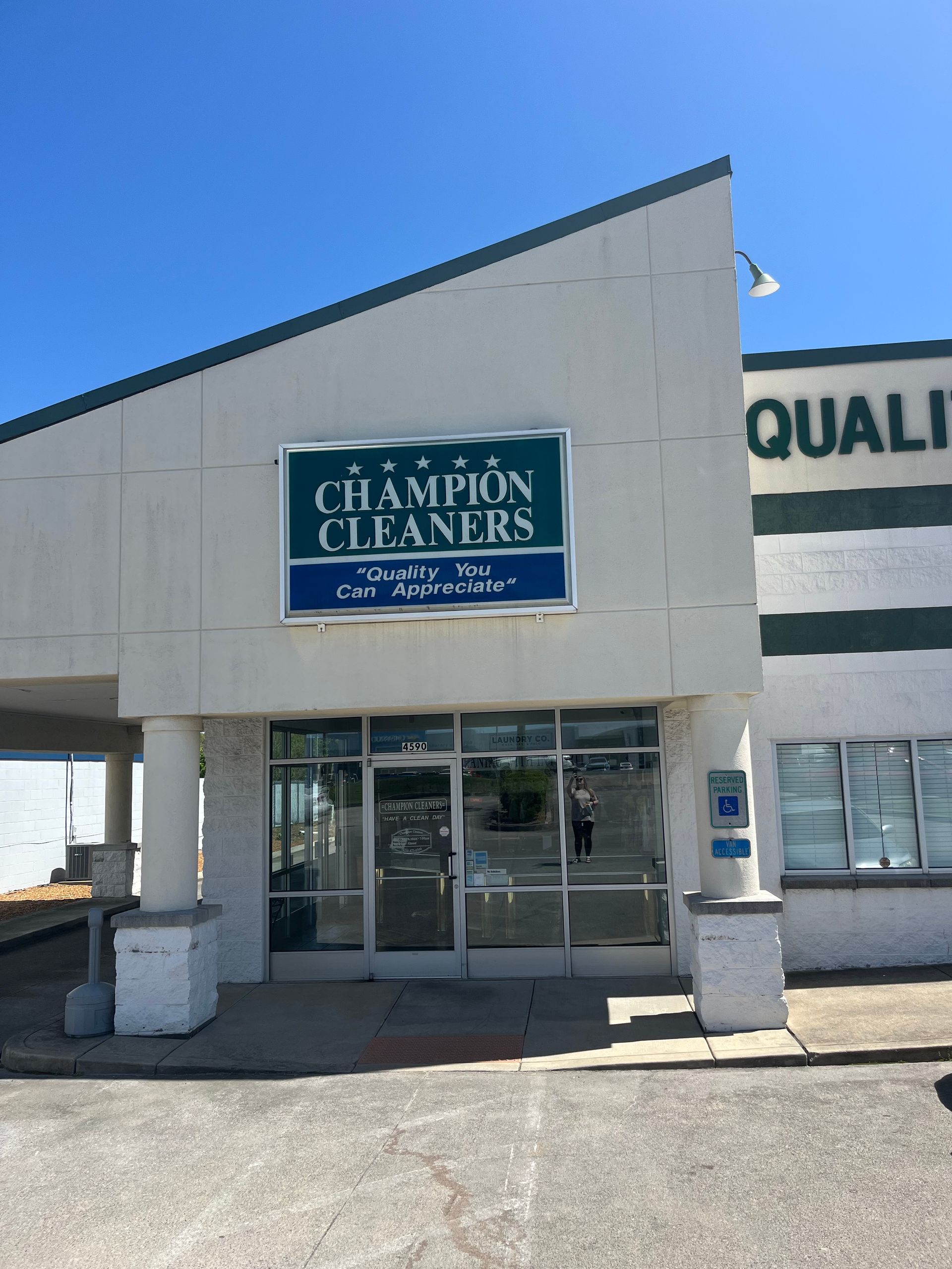 Champion Cleaners storefront with blue sign. White building, glass door, and blue sky.