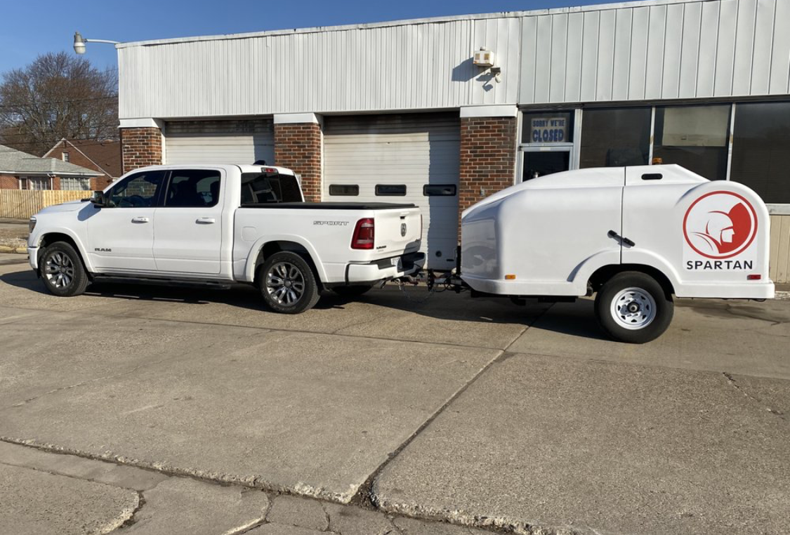 A white truck with a trailer attached to it is parked in front of a building.