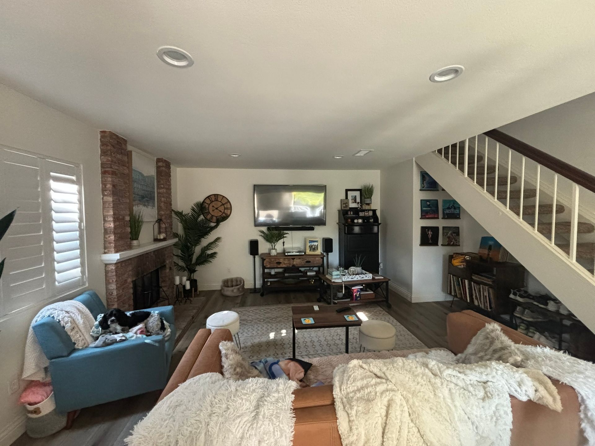 Living room with blue armchair, tan sofa, brick fireplace, television, and a staircase leading to an upper level.