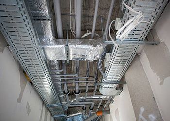 Construction view of exposed cables, pipes, and ventilation systems in a ceiling cavity.