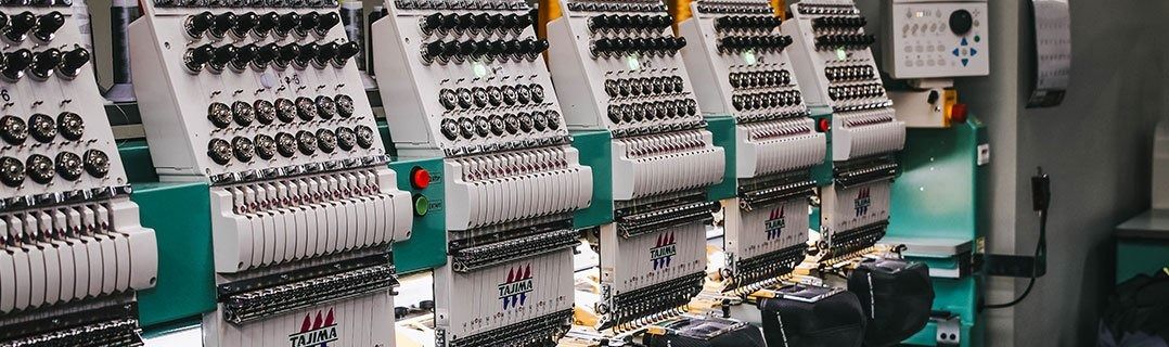 Multi-head industrial embroidery machine with thread spools and needles in a manufacturing facility.