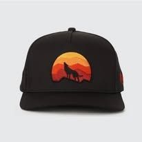 A black baseball cap featuring an embroidered design of a wolf howling at a sunset over layered mountains.