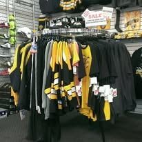 A retail rack displays Boston Bruins hockey jerseys and apparel in black and yellow, with a small sale sign overhead.